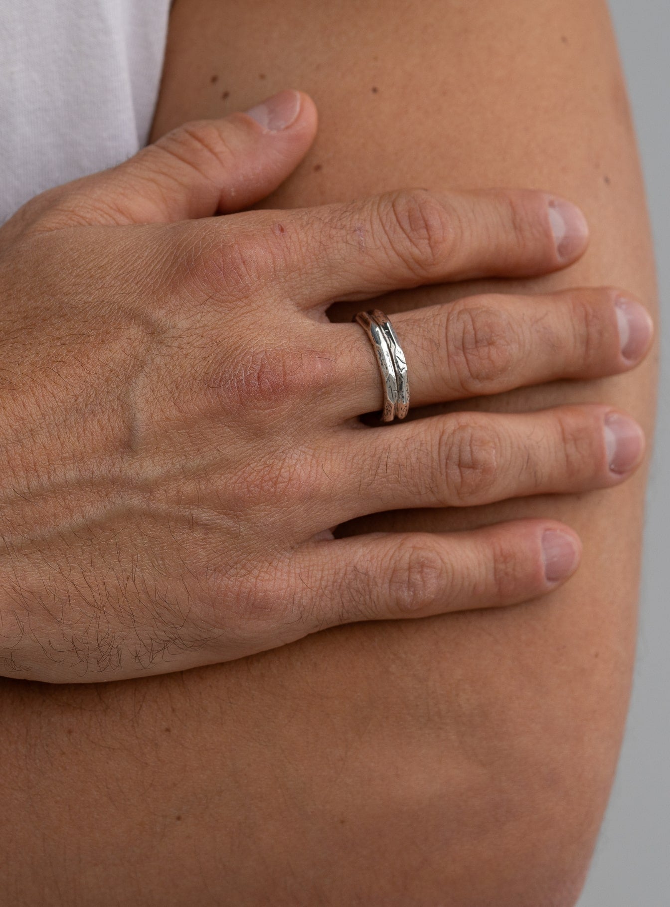 Close-up of a hand resting on the arm, featuring a textured sterling silver ring with a rugged and minimalist design, complementing a casual, modern look.